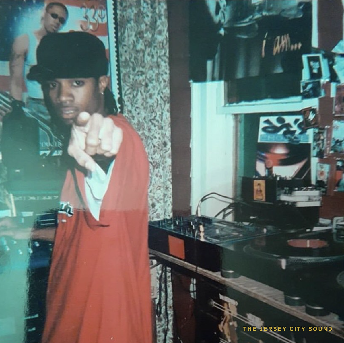 DJ E Double pointing at the camera beside turntables and a mixer
