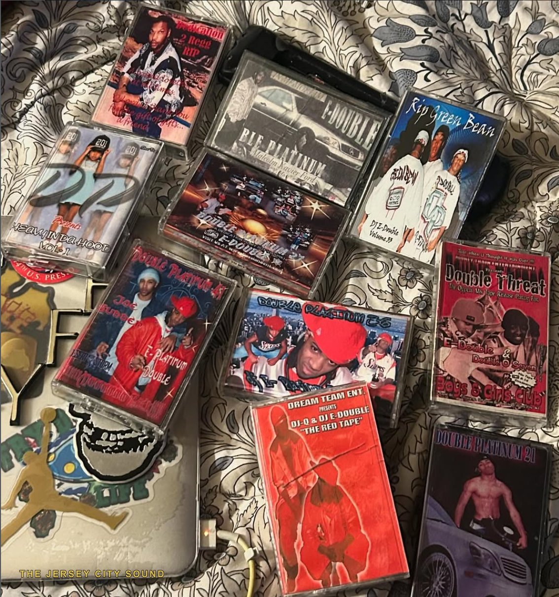 A spread of DJ E Double mixtape cassettes including Double Platinum volumes and memorial tapes