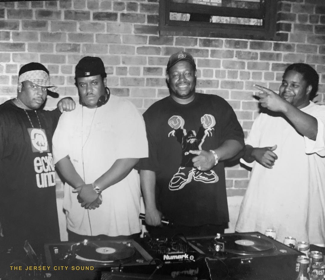 Joey Times, DJ Wimpy Bee, DJ Flash, and DJ Tysheem behind turntables at a brick walled room