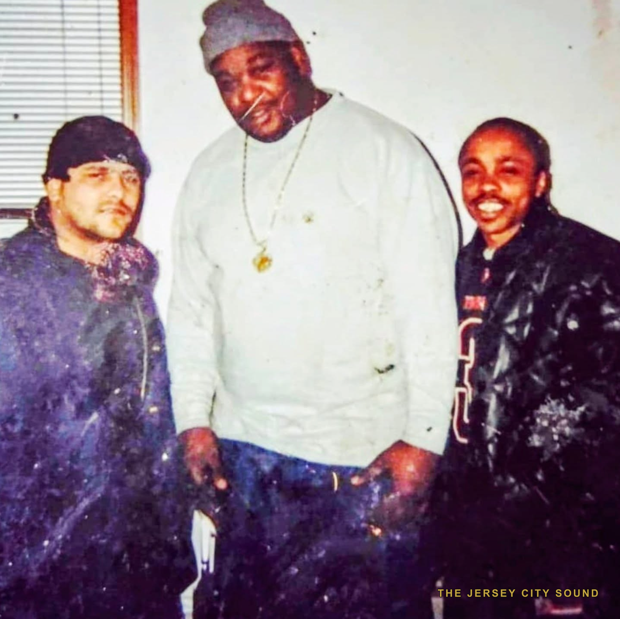 Double J in a knit cap and chain standing between two friends