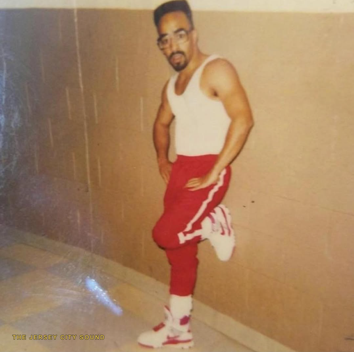 Lord Sun Albee Al posed in a hallway in a white tank top and red track pants