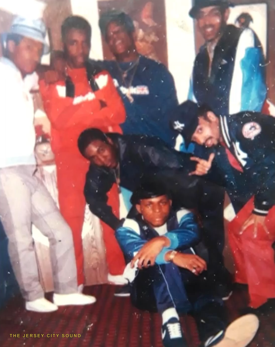 Seven members of the crew posed in a room in 1980s tracksuits and Yankees gear