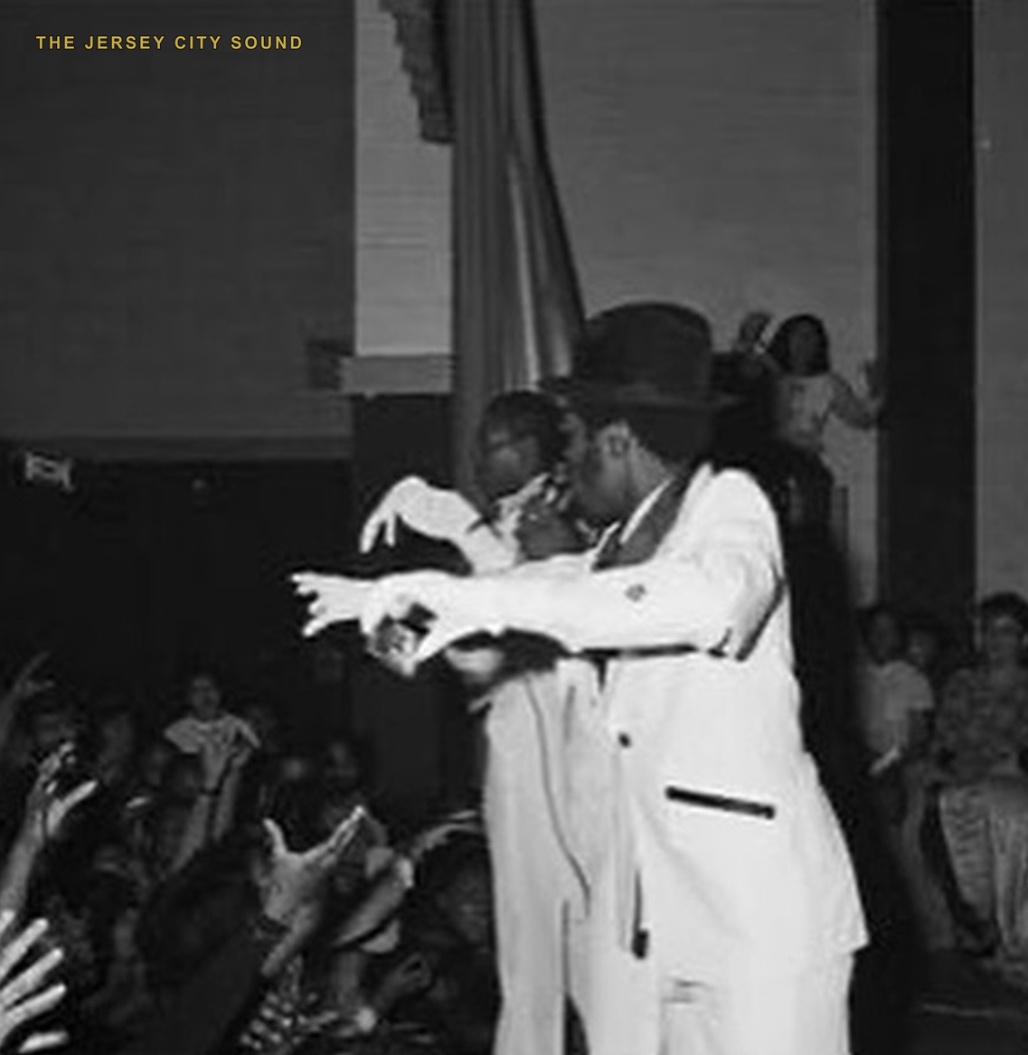 Two performers in white suits reaching over a crowd on stage